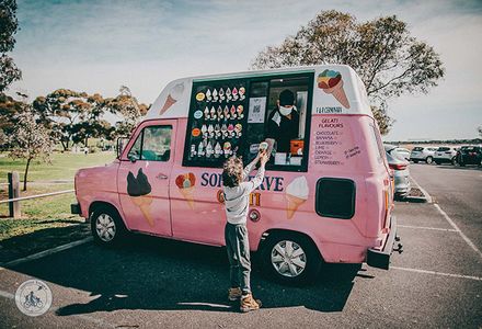 A young boy buys an icecream from a bright pink icecream van at the beach.