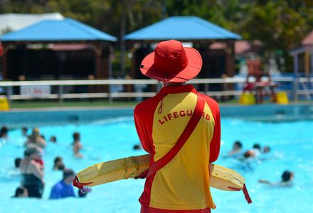 A lifeguard supervises children swimming in a sunny outdoor pool.