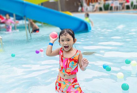 A cheerful girl enjoys playing with pool toys after sliding down a waterslide.