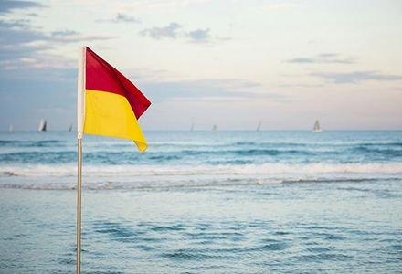 A red and yellow flag flaps in the wind at an Australian beach.