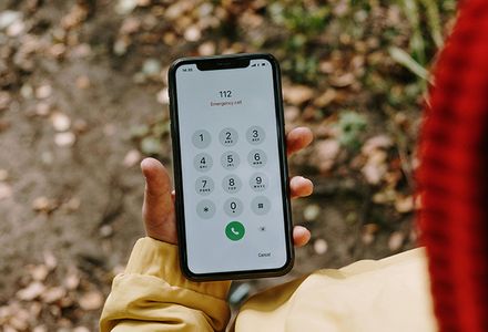A person holding a smartphone displaying the number triple zero on the screen, ready to make a call.