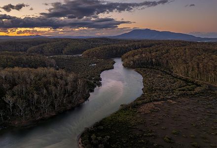 A river twists through the landscape surrounded by trees and lit by a setting sun.