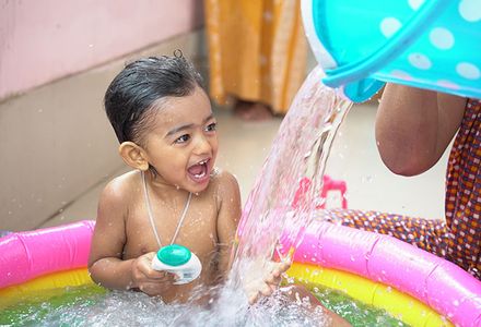 A toddler laughs and plays in a brigh paddling pool.
