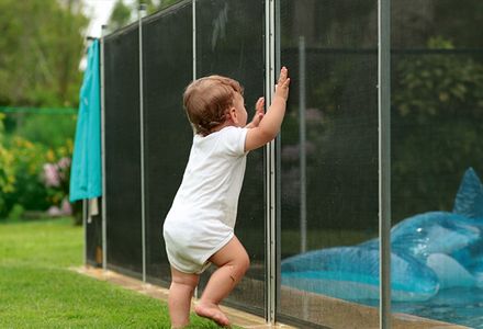A baby leans on a pool fence, trying to get access to a swimming pool.